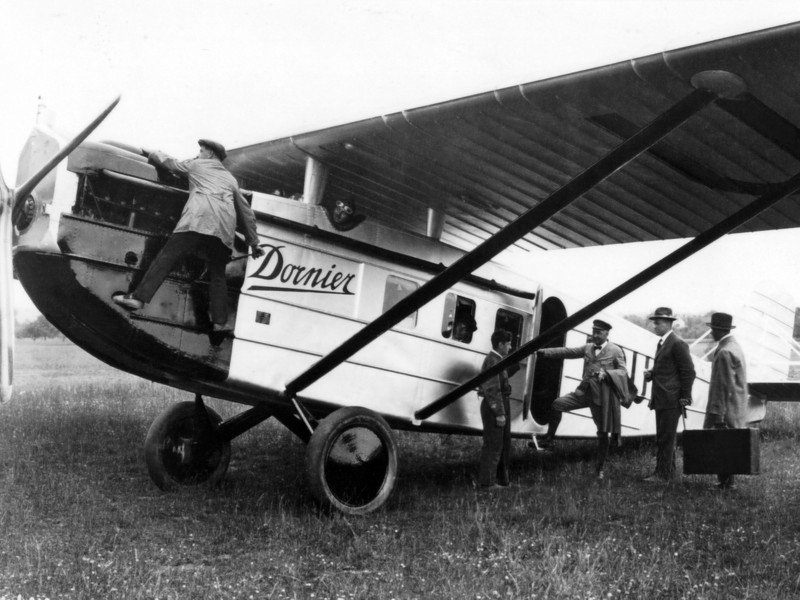 Historisches Schwarz-Weiß-Foto von Menschen, die über eine Treppe in ein Flugzeug der 1920er-Jahre einsteigen