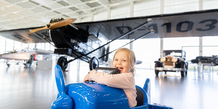 Kleines Mädchen sitzt in blauem Spielzeugflugzeug