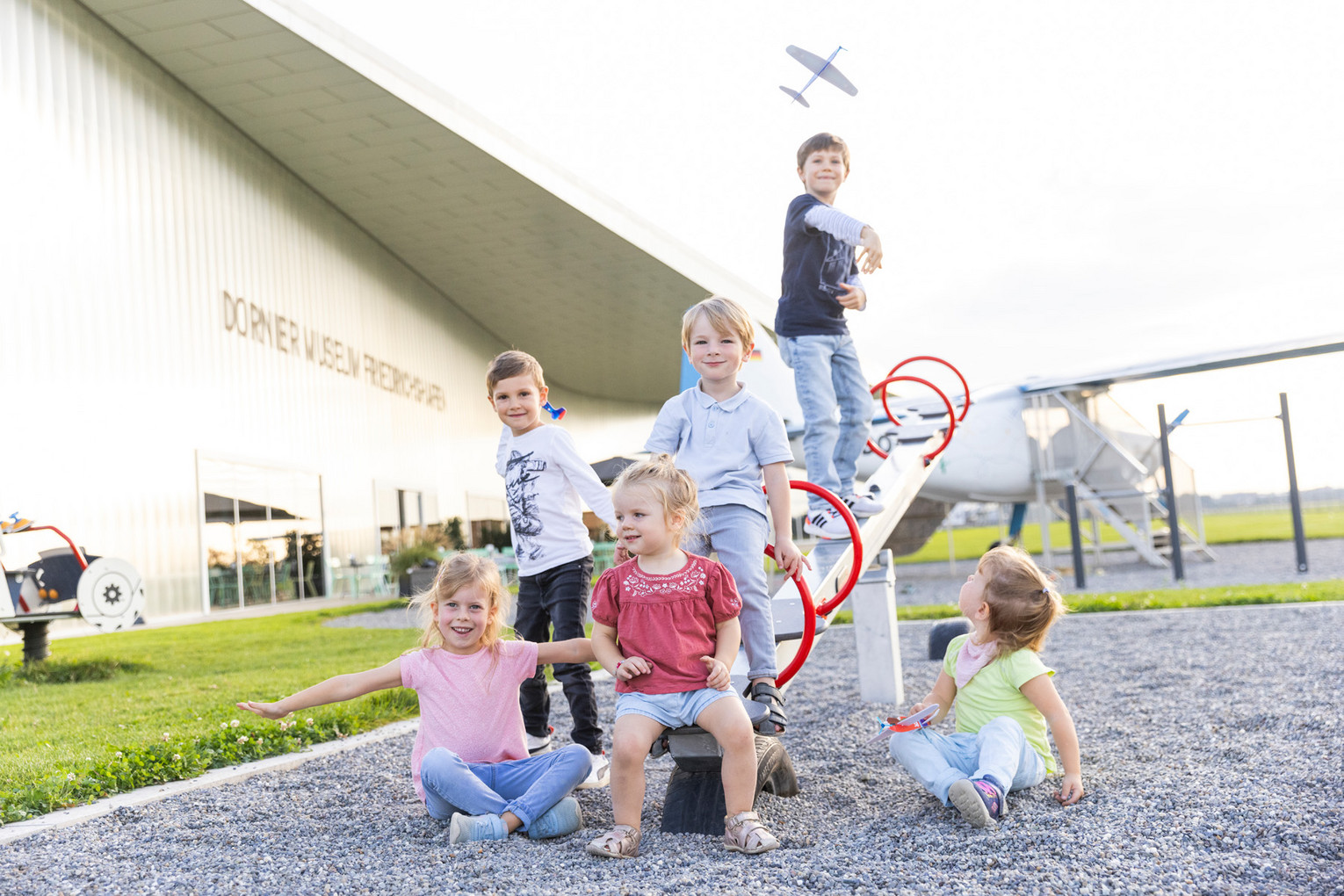Mehrere Kinder spielen auf einer Wippe auf dem Spielplatz direkt neben dem Rollfeld.