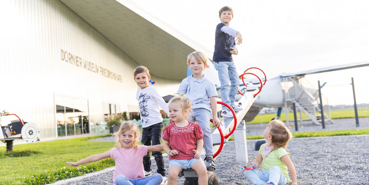 Mehrere Kinder spielen auf einer Wippe auf dem Spielplatz direkt neben dem Rollfeld.