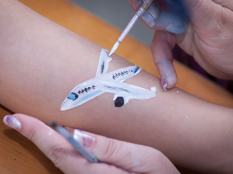 Ein Flugzeugmotiv wird auf einen Arm gemalt.