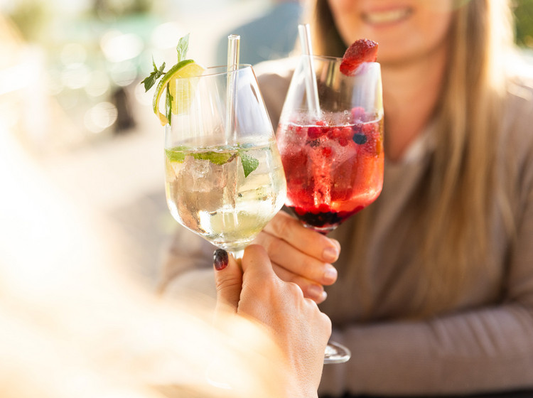 Zwei Frauen stoßen mit Cocktails an und lächeln sich dabei an.