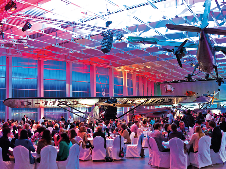 Personen sitzen an Tischen, im Hangar um eine Veranstaltung zu genießen.
