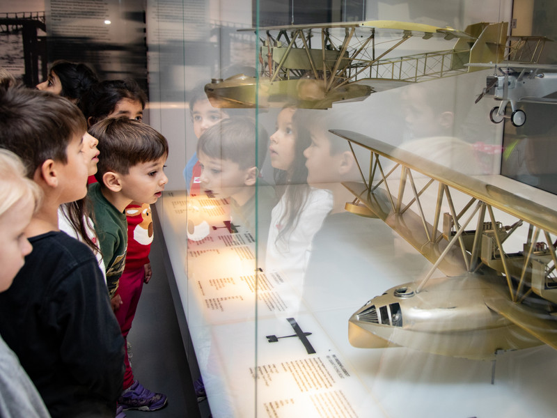 Mehrere Personen stehen vor einer gläsernen Vitrine im Museum und betrachten Modelle und technische Exponate