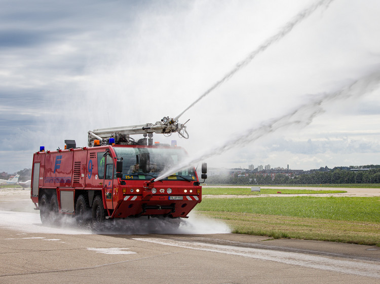 Ein Flughafen-Feuerwehrfahrzeug spritzt Wasser auf das Rollfeld.