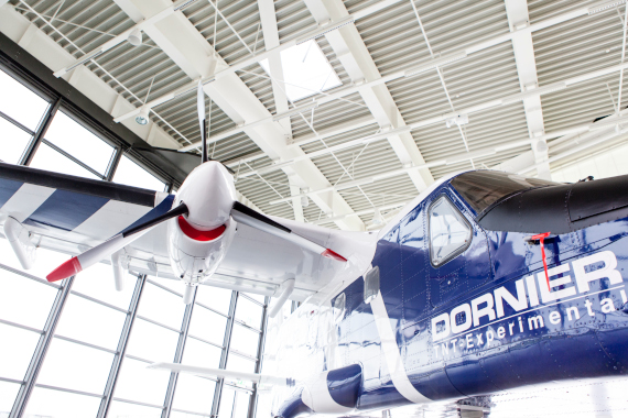 Innenansicht einer Ausstellungshalle mit aufgehängtem Flugzeugmodell in Blau mit der Aufschrift „Dornier“, modernes Hallendach und große Fenster im Hintergrund.